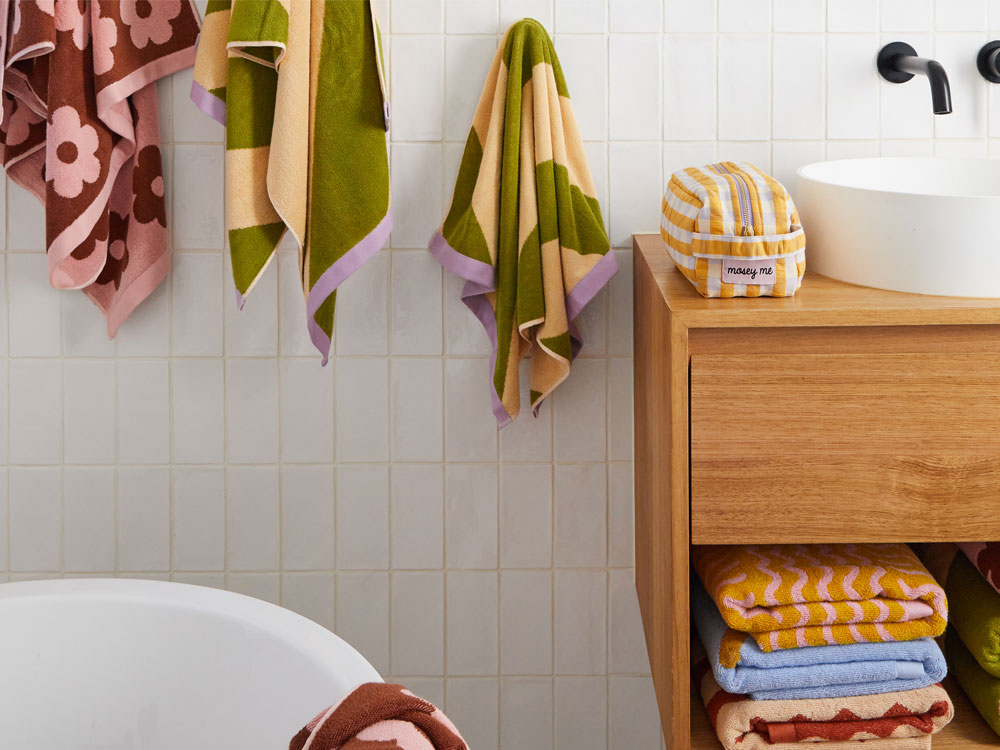 Bathroom with colorful towels hanging and stacked on a wooden cabinet.