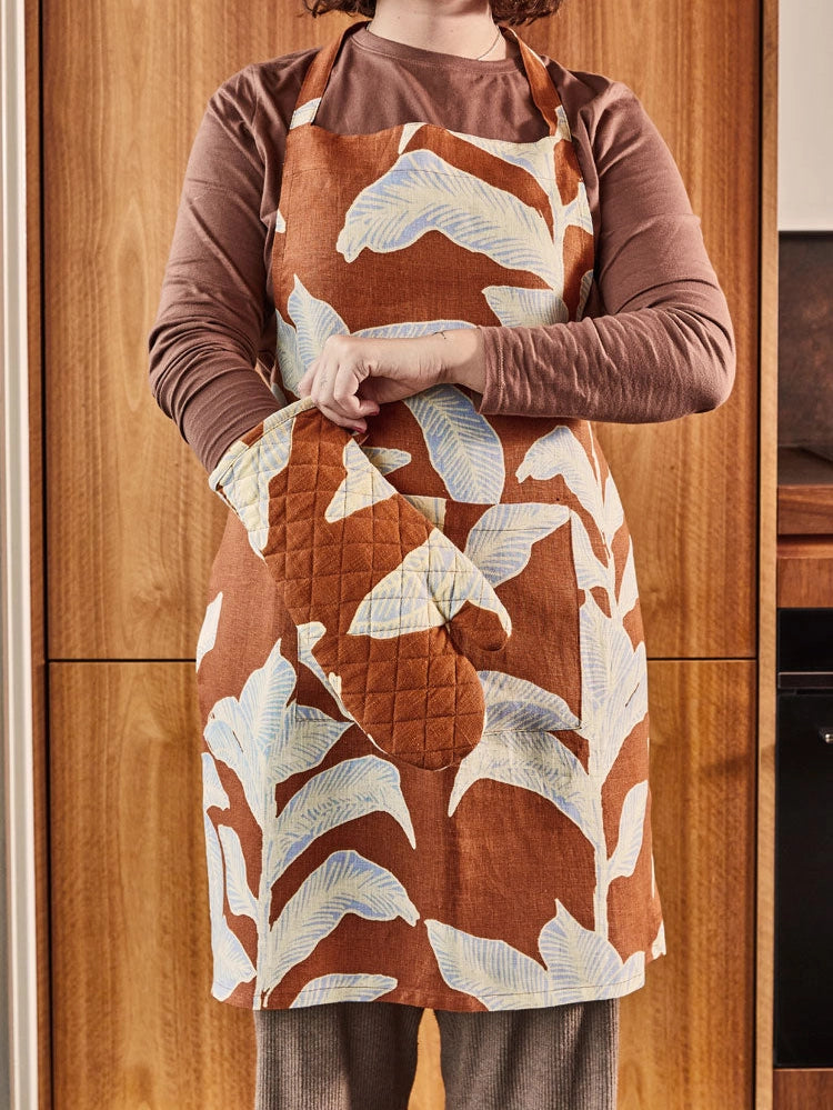 Person wearing a brown apron with leaf pattern in a kitchen setting