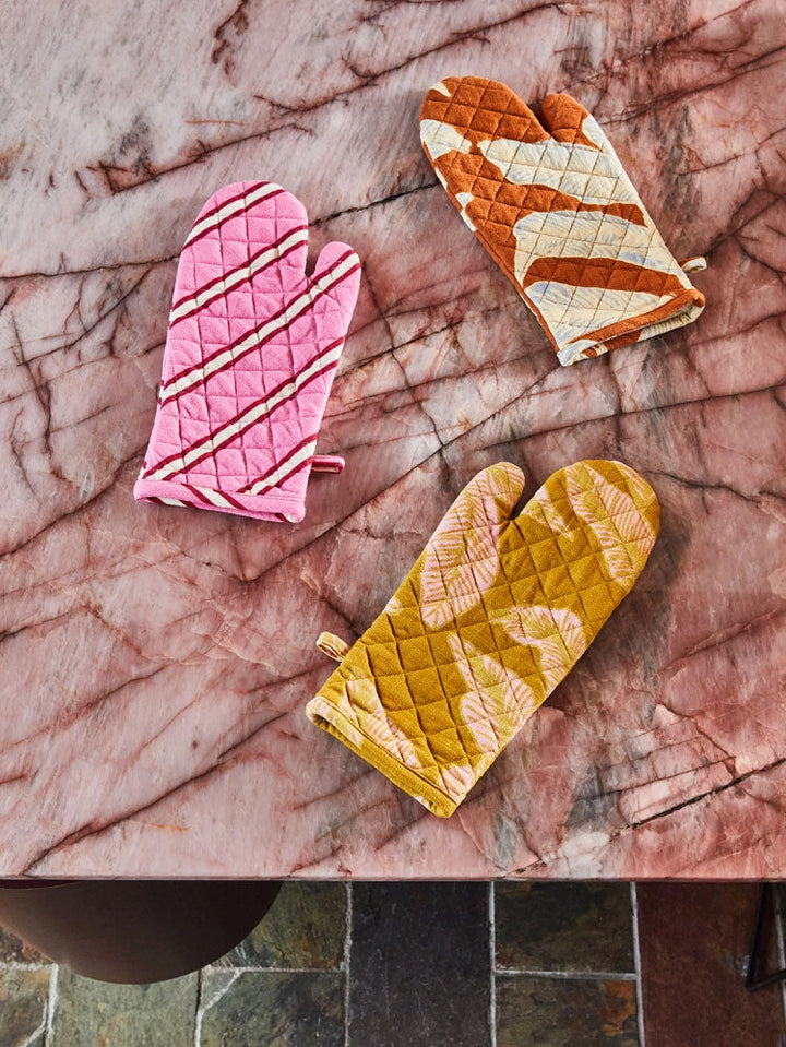 Three patterned oven mitts on a marble surface