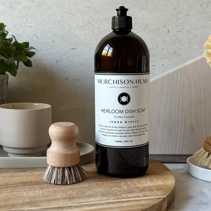Murchison-Hume heirloom dish soap bottle on a wooden surface with a brush and plant in the background.