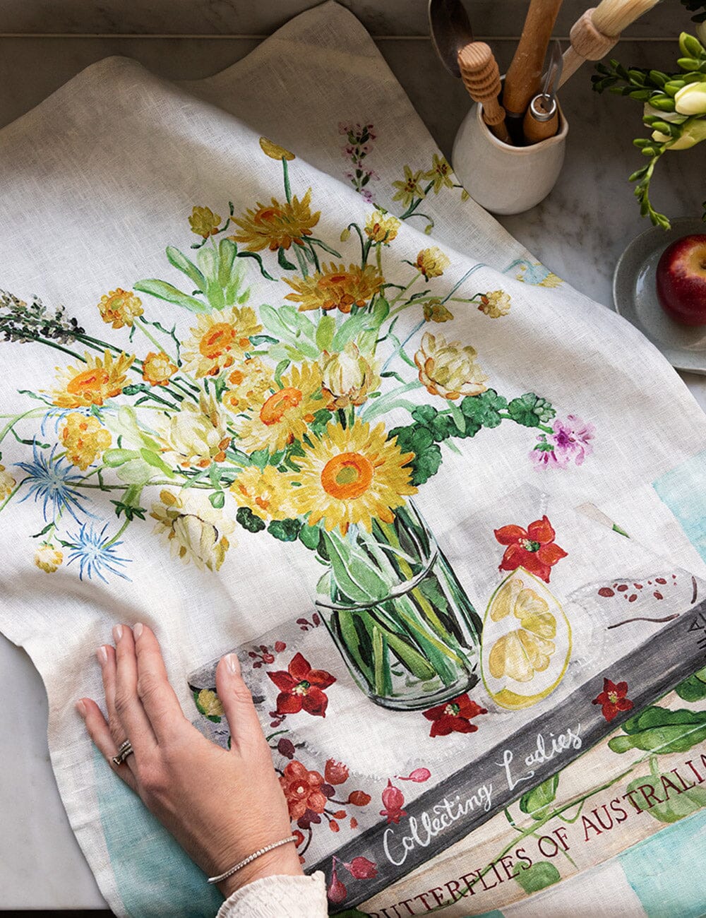 Floral design on a towel with a hand touching it, set against a kitchen counter.