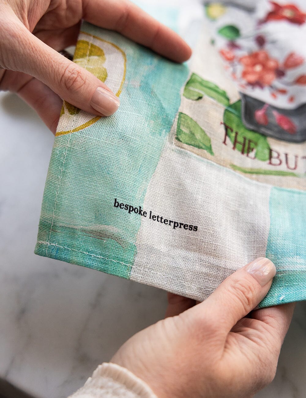 Hand holding a linen tea towel with 'bespoke letterpress' text.