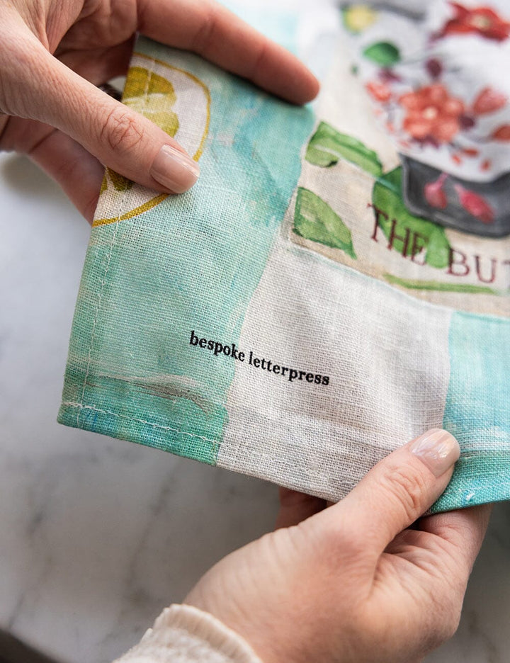 Hand holding a linen tea towel with 'bespoke letterpress' text.