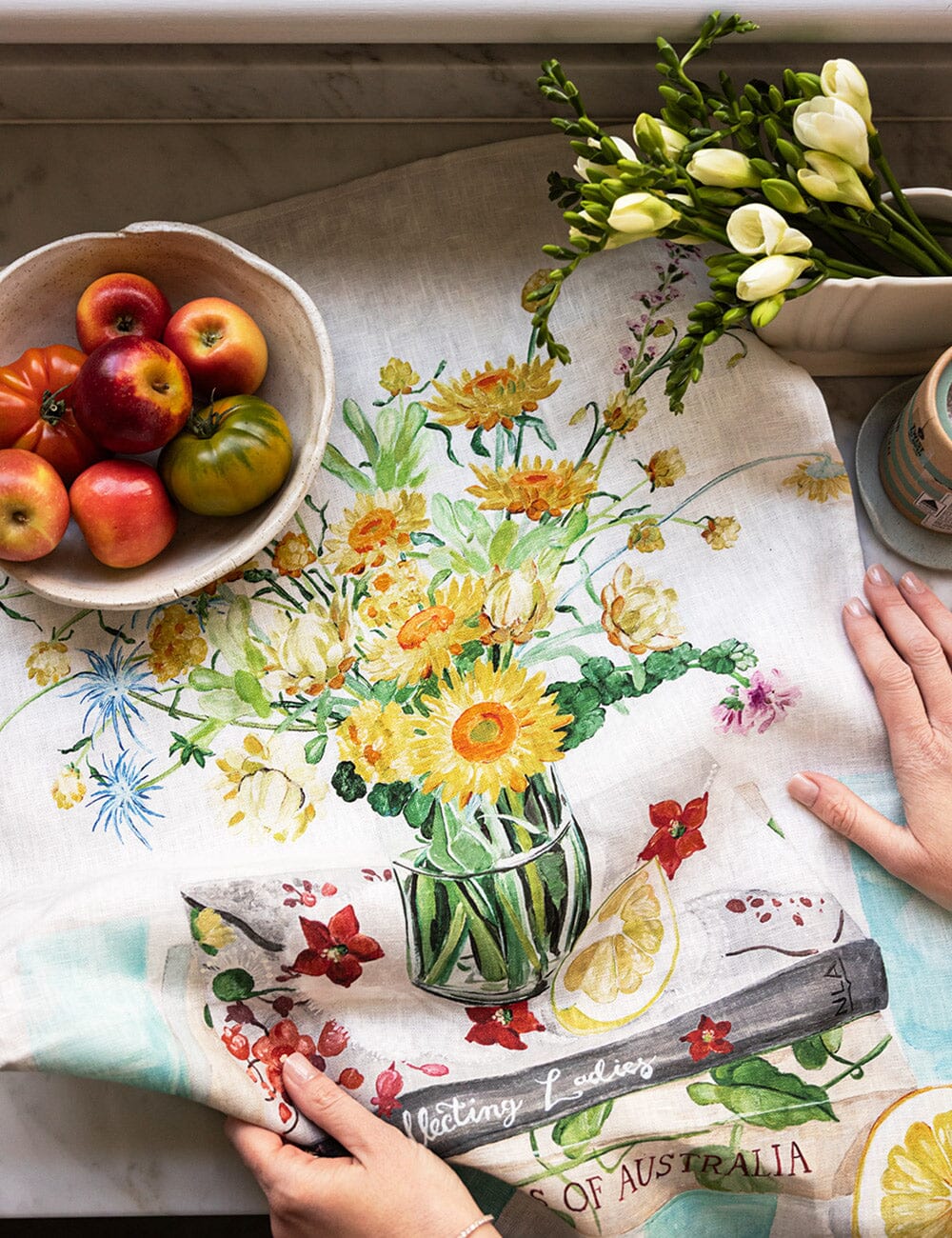 Floral-themed kitchen towel with a bowl of apples and flowers on a table.
