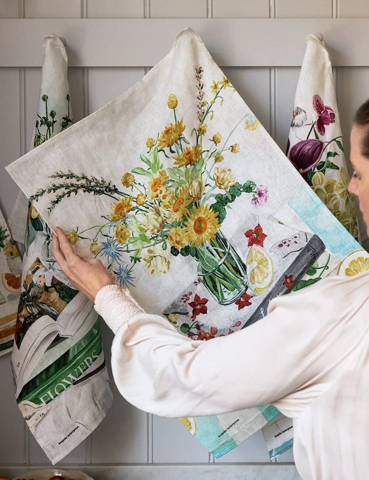 Person holding a floral-themed kitchen towel with a decorative background