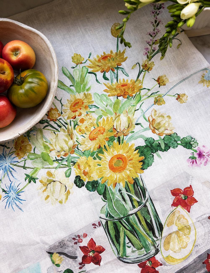 Floral design on a tablecloth with a bowl of apples and tomatoes.