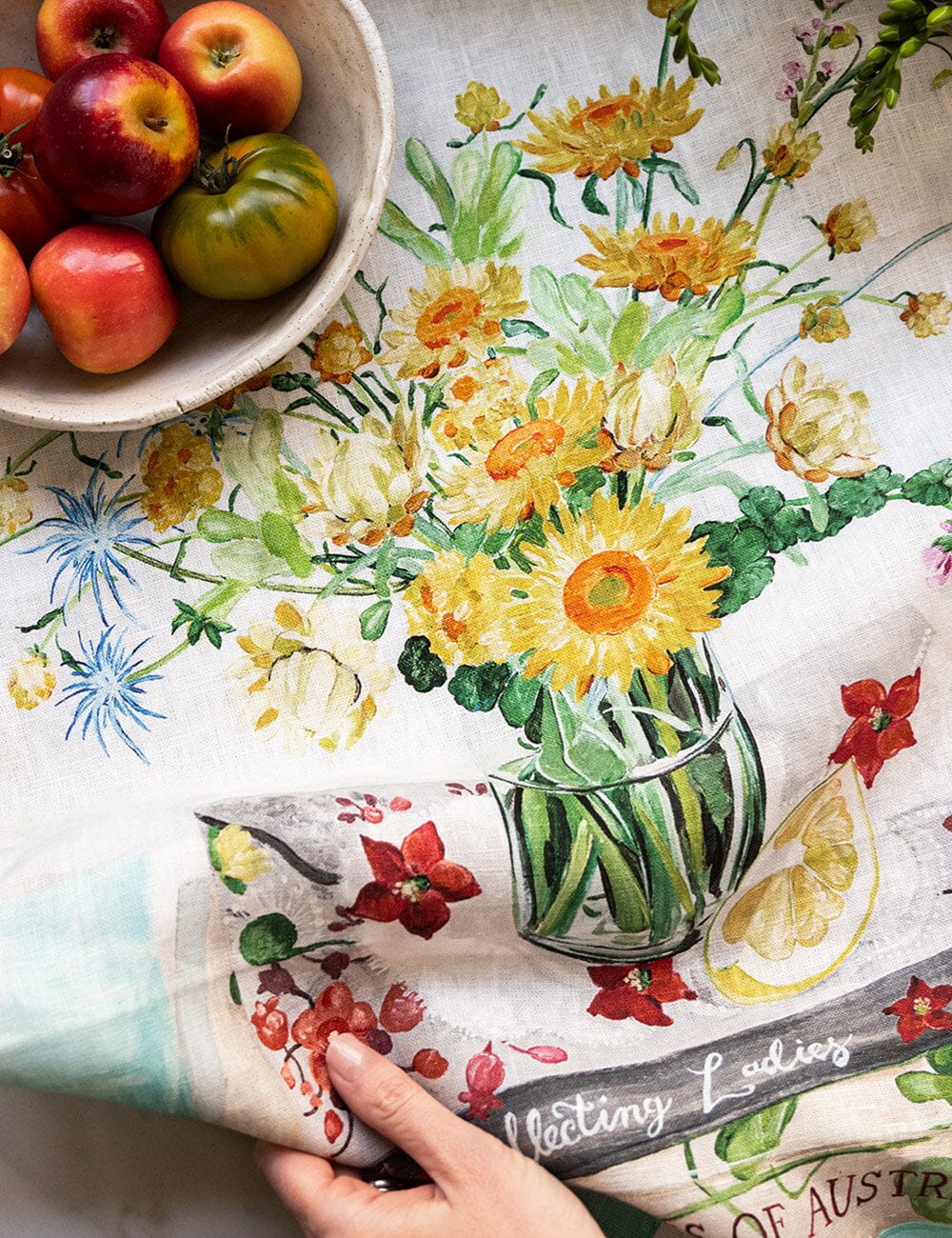 Floral tablecloth with a bowl of apples and a glass vase on a table.
