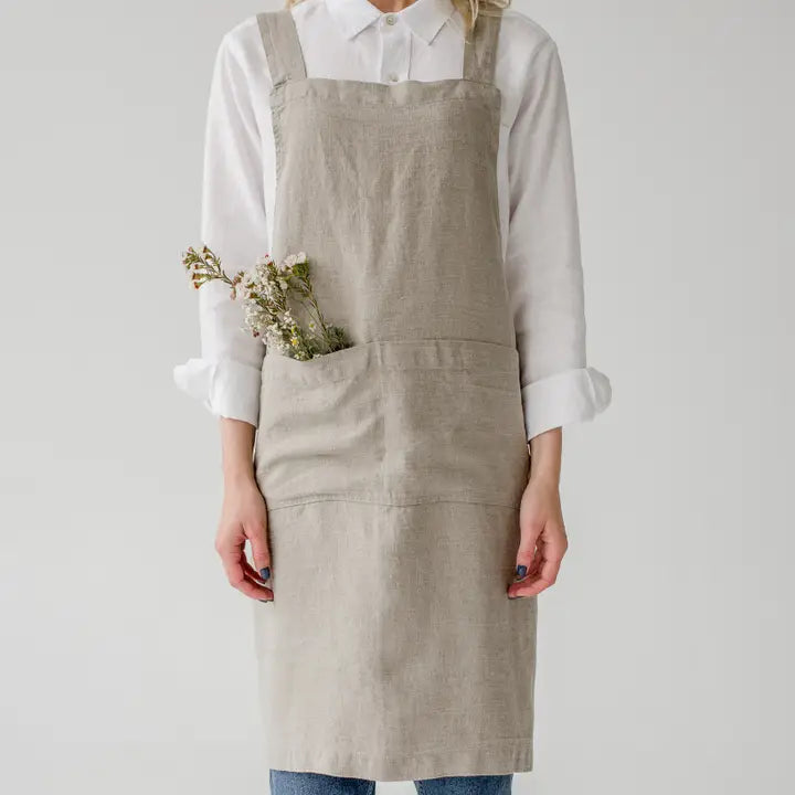 Person wearing a beige apron holding dried flowers on a plain background
