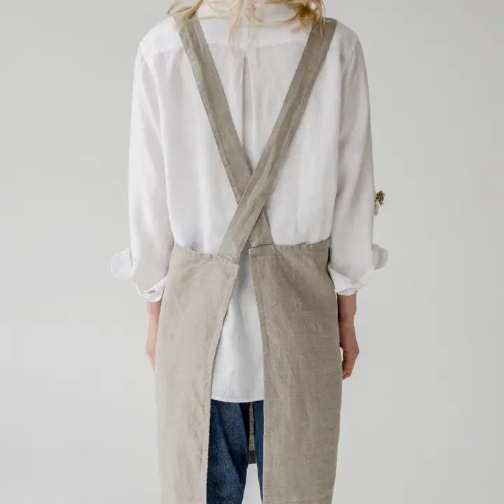 Person wearing a beige apron over a white shirt on a plain background