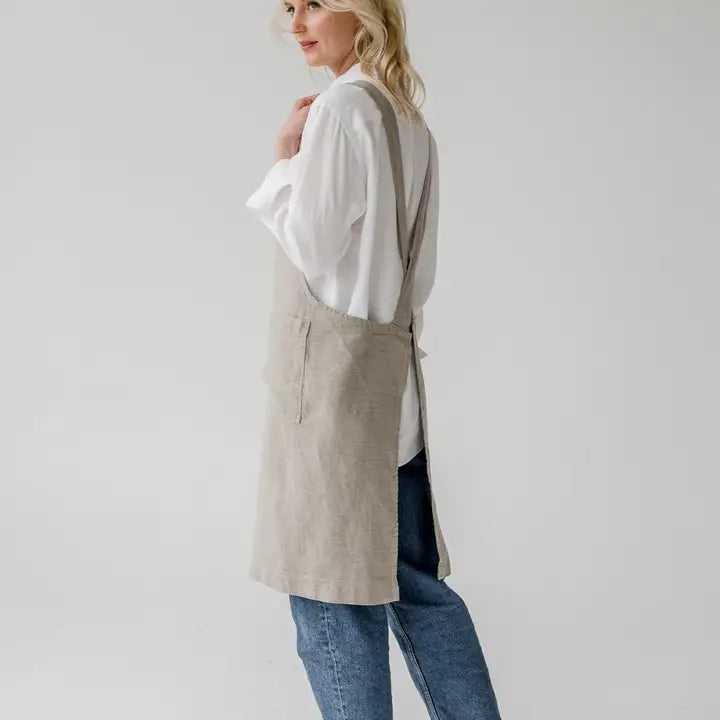 Woman wearing a beige apron over a white shirt and blue jeans on a plain background