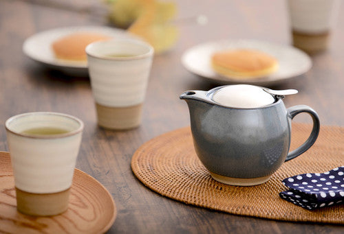 Ceramic teapot and cups on a wooden table with plates of food in the background