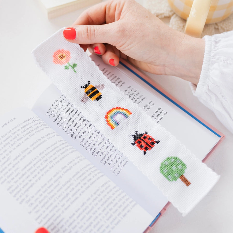 Cross-stitched bookmark with colorful designs held over an open book