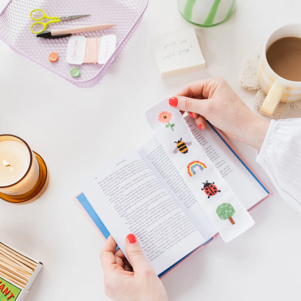 Person holding a book with illustrated pages on a desk with stationery items.
