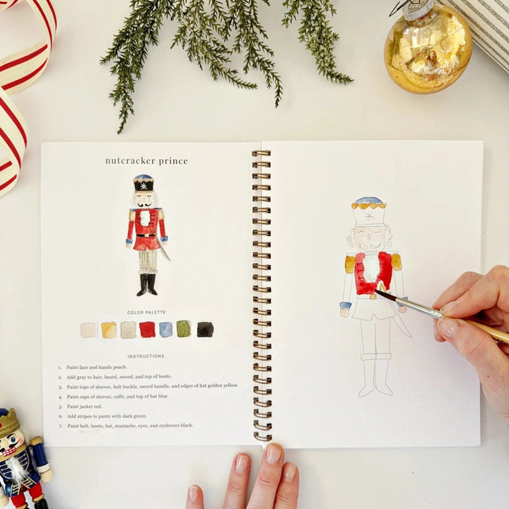 Open watercolour workbook, with a hand panting a Nutcracker