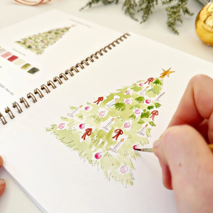 Person drawing a Christmas tree on a spiral-bound notebook with a pen.