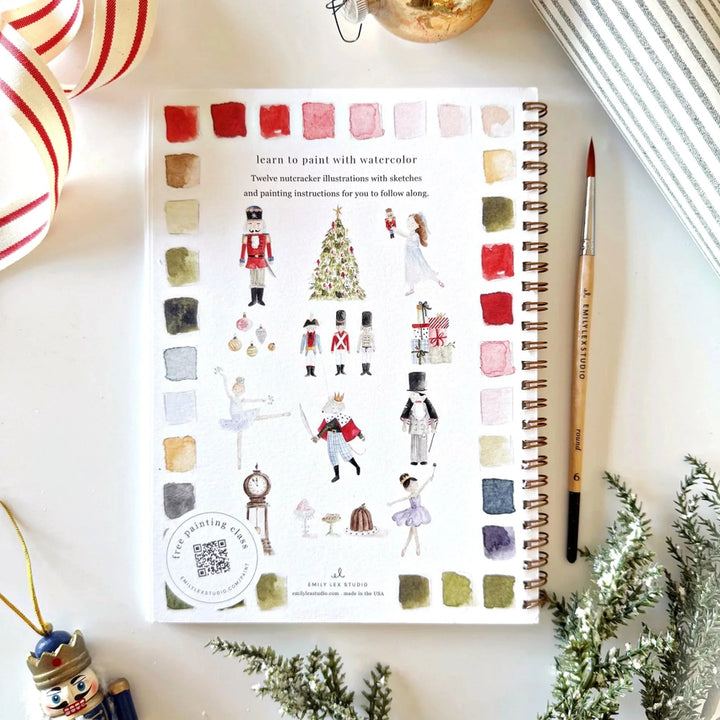 An Emily Lex watercolor workbook with  illustrations on a decorative surface with Christmas decorations.