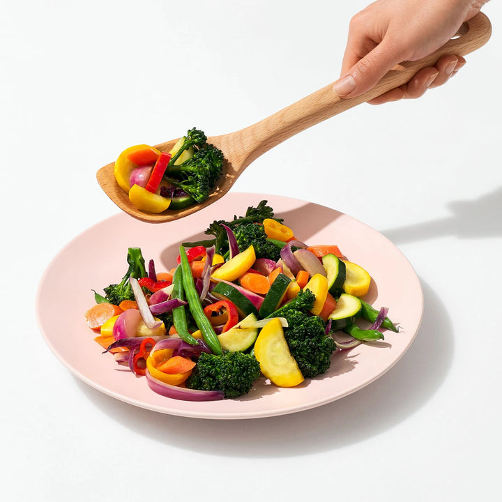 Colorful salad on a pink plate with a wooden spoon, on a white background