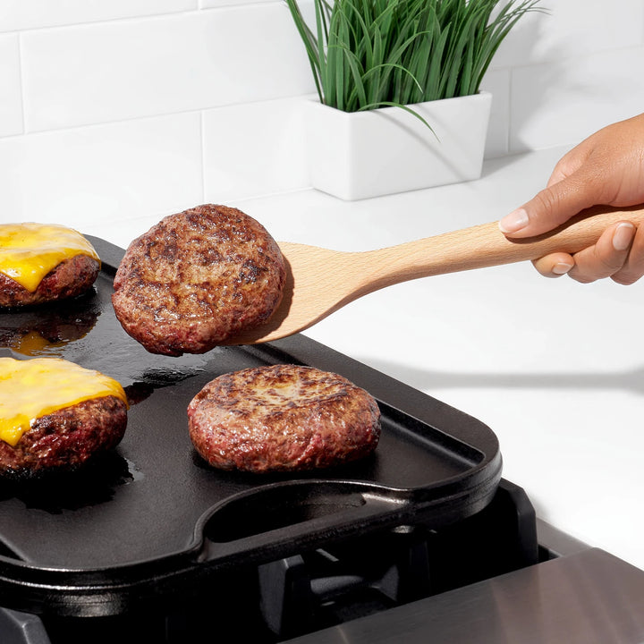 Hamburgers being cooked on a grill with a wooden spatula, white kitchen background.