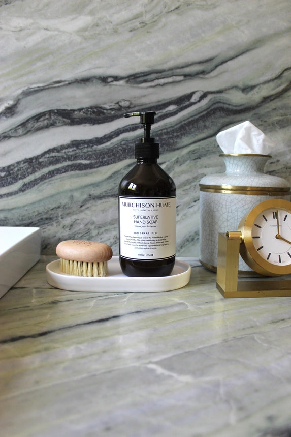 Bottle of hand soap on a marble surface with a clock and tissue paper holder.
