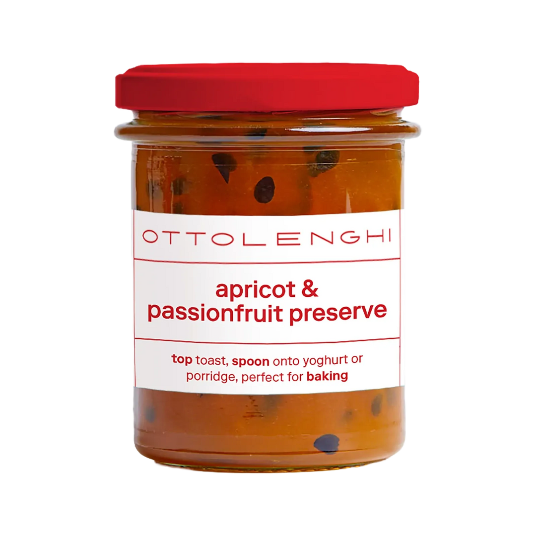 A glass jar of Ottolenghi apricot &amp; passionfruit preserve with a bright red lid and a white label, shown on a plain white background.