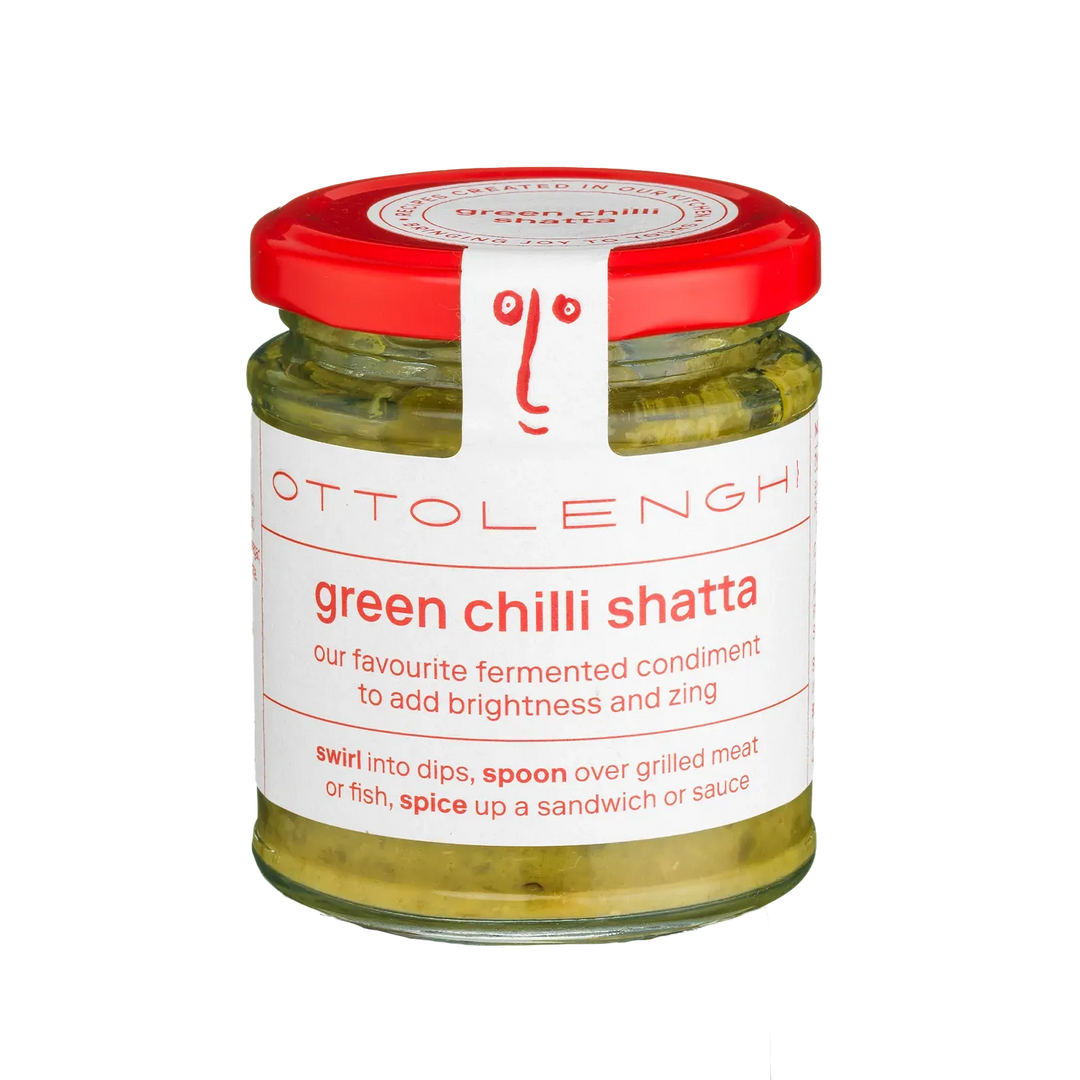 A glass jar of Ottolenghi Green Chilli Shatta condiment, featuring a white label with red text and a red lid, set against a plain white background.