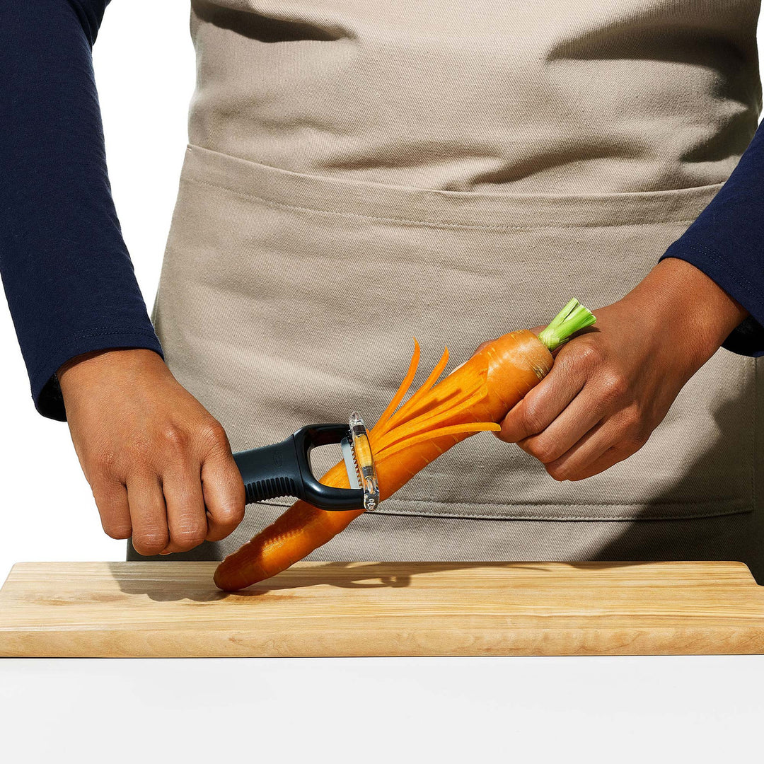 Person peeling a carrot with a vegetable peeler on a wooden cutting board.