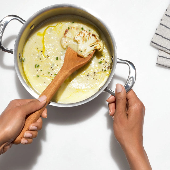 Person stirring creamy cauliflower soup with a wooden spoon in a pot.