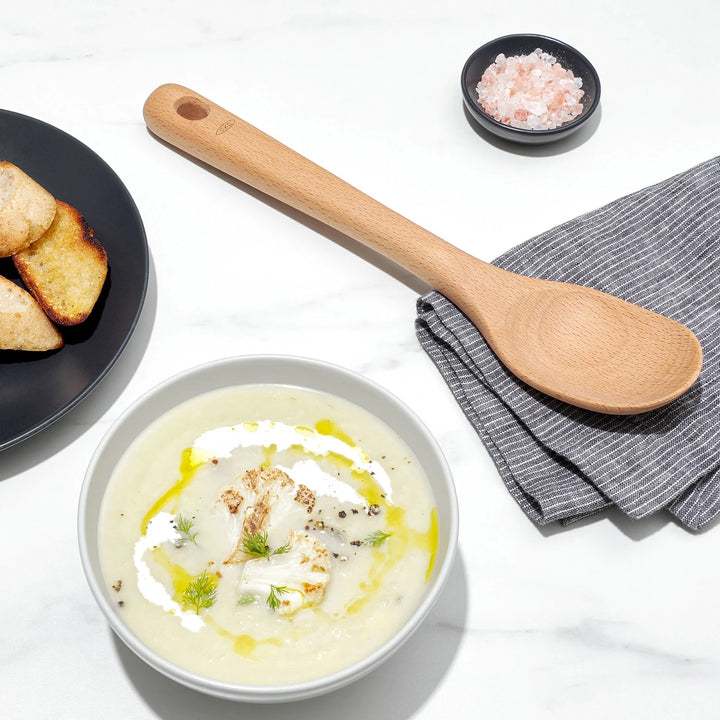  bowl of soup with a wooden spoon and bread on a white background