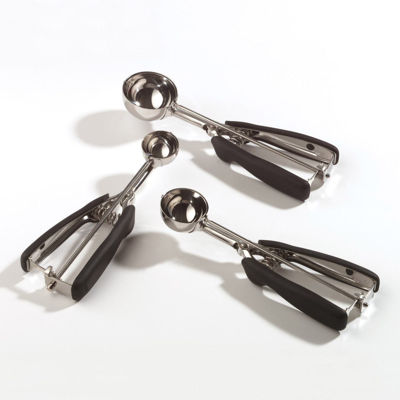 Set of four metal cookie scoopers with black handles on a white background