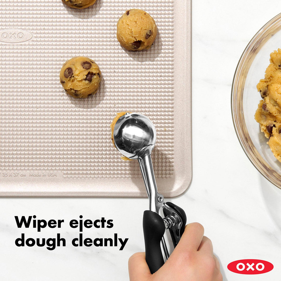 OXO cookie scoop with cookies on a baking sheet and a bowl of cookies.