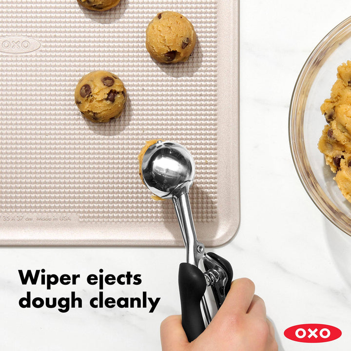 OXO cookie scoop with cookies on a baking sheet and a bowl of cookies.
