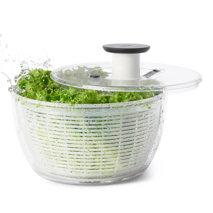 Clear salad spinner with fresh greens on a white background