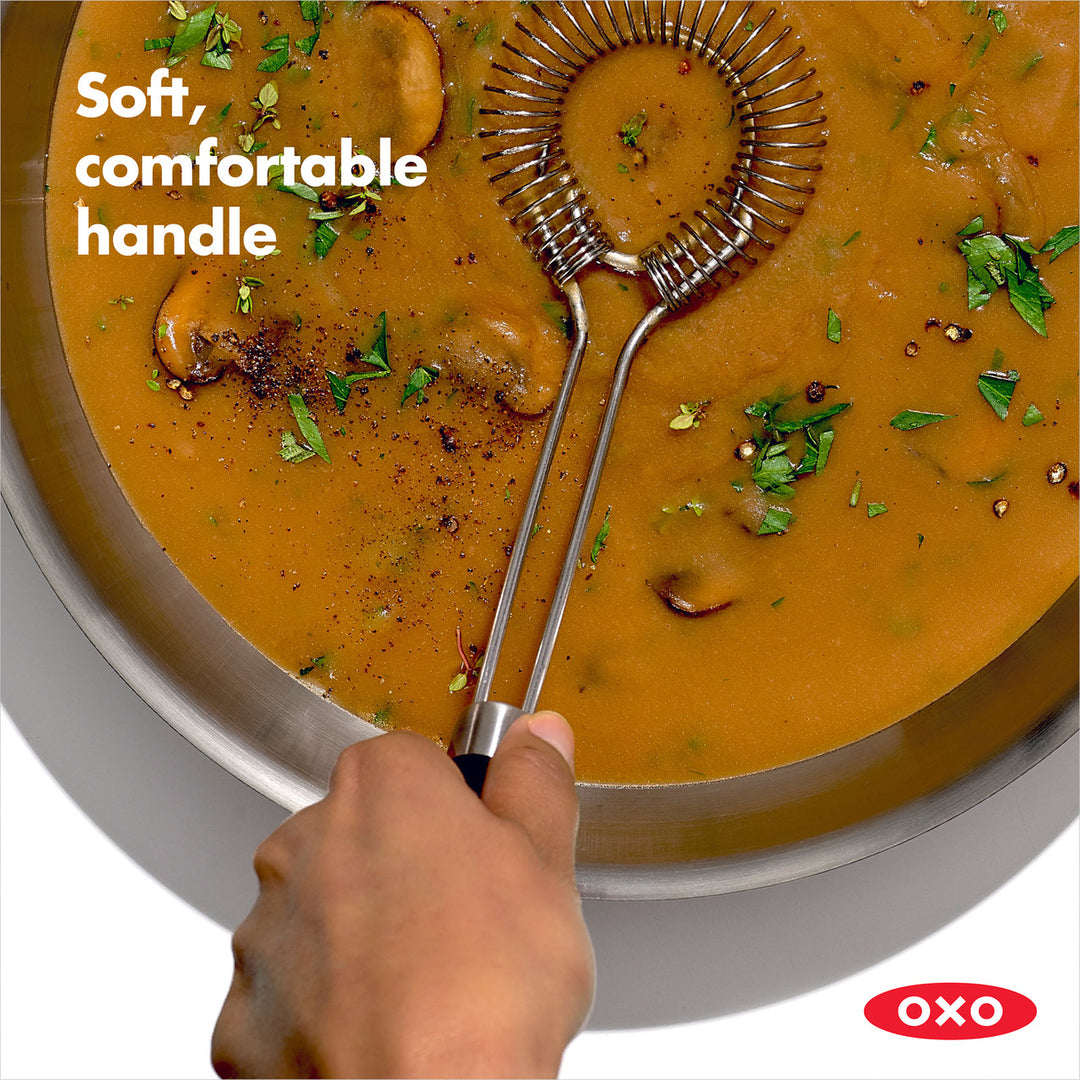 Metallic sauce and gravy whisk being used to stir a pot of soup with text &