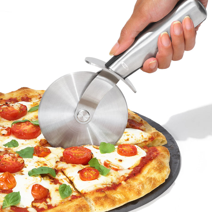 Person using a pizza cutter to slice a pizza with various toppings on a white background