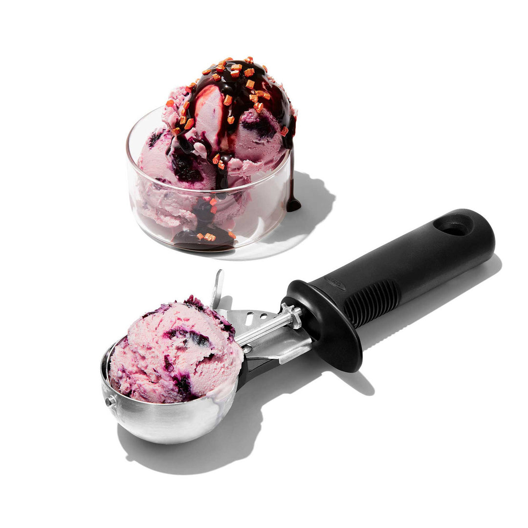 Ice cream scoop with a scoop of pink ice cream next to a bowl of ice cream on a white background