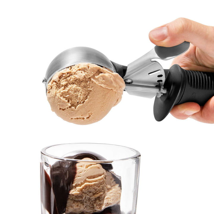 Ice cream scoop with a scoop of ice cream being placed into a glass.