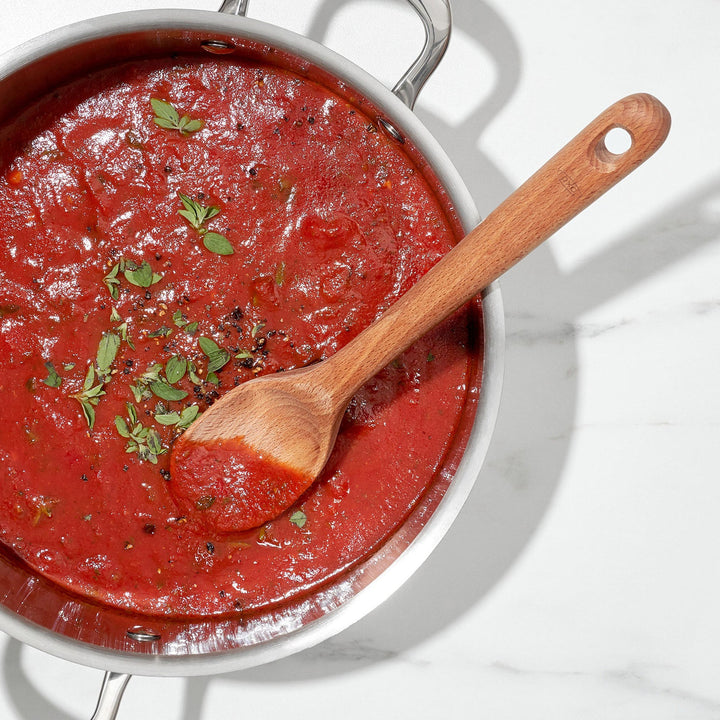 Red sauce in a pan with a wooden spoon on a white background