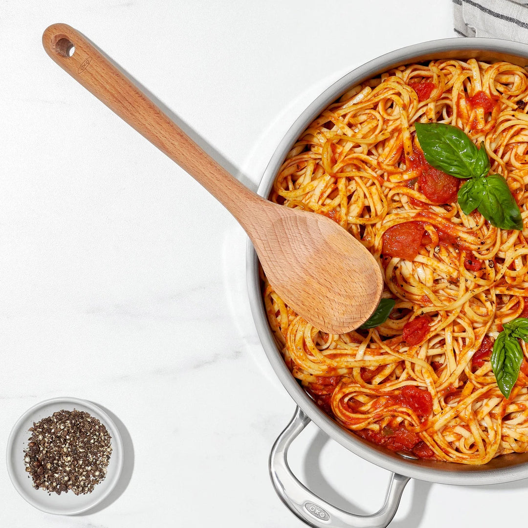 Pasta dish with a wooden spoon in a white pan on a light background