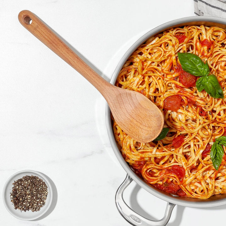 Pasta dish with a wooden spoon in a white pan on a light background