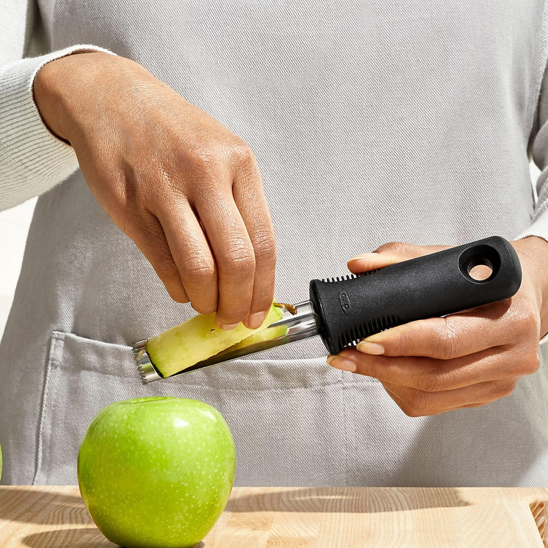 Person using a kitchen peeler on a green apple with a neutral background