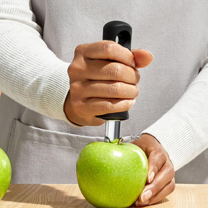 Person using an apple corer on a green apple with a neutral background