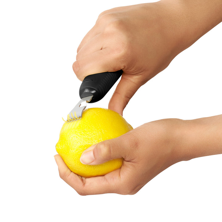 Hand using a lemon peeler to remove the skin of a lemon on a white background