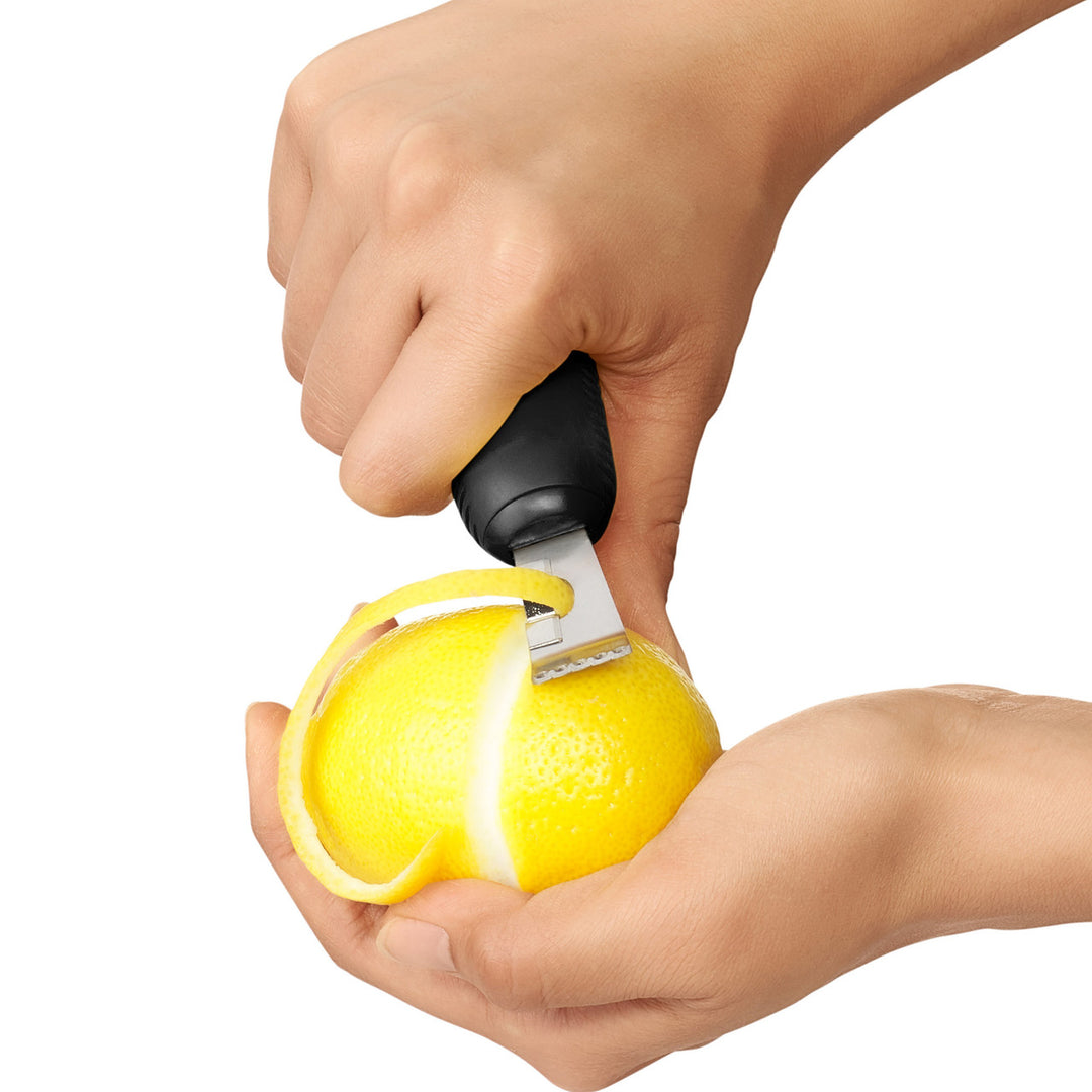 Hand using a citrus zester on a lemon against a white background