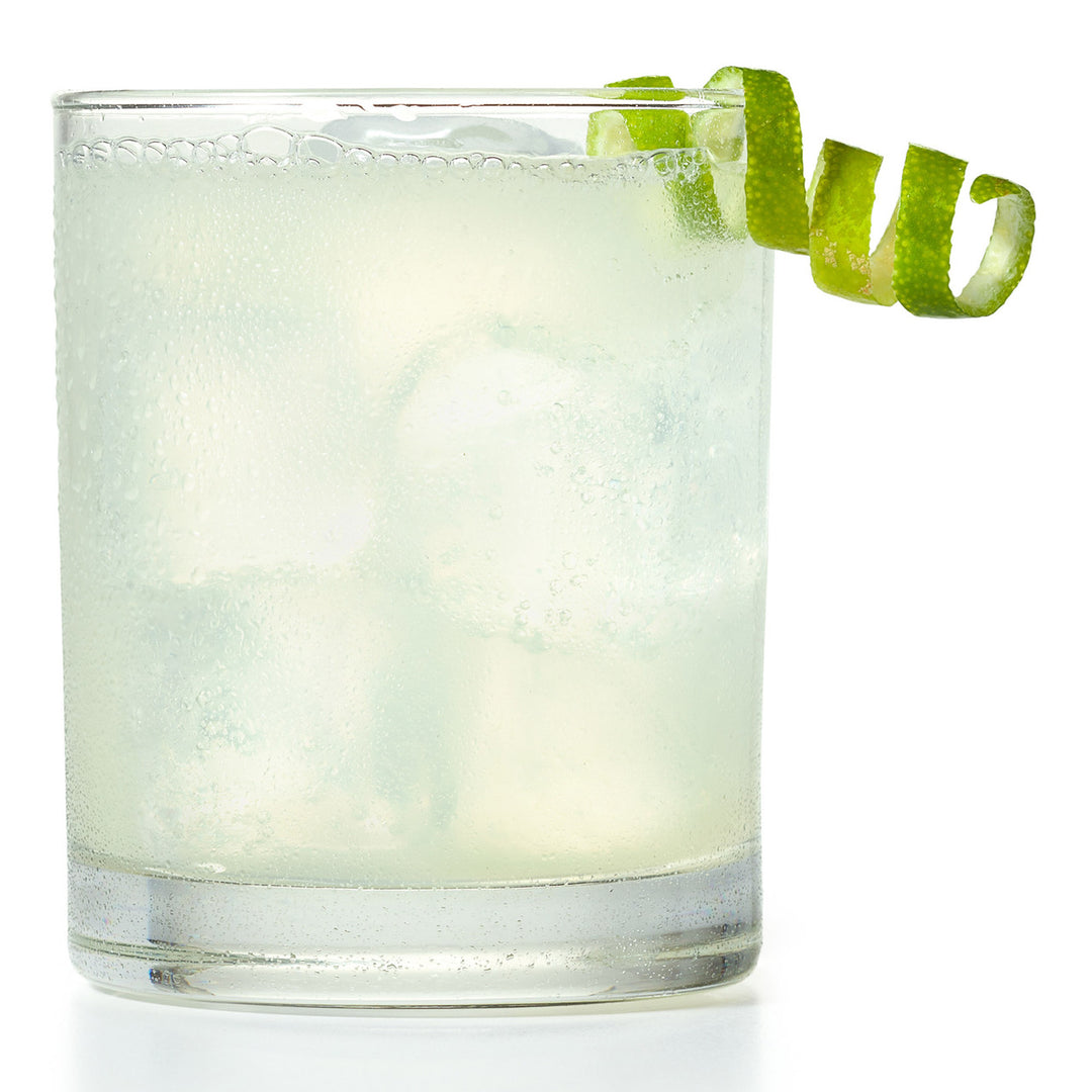 Glass of a light-colored cocktail with a lime twist on a white background