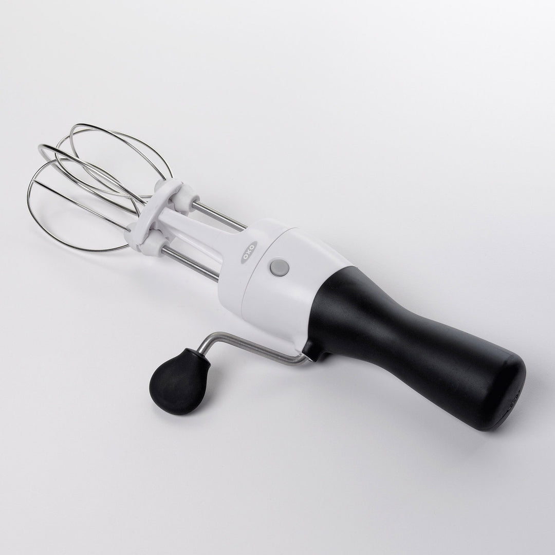 Egg beater with black handle and silver whisk attachment on a white background