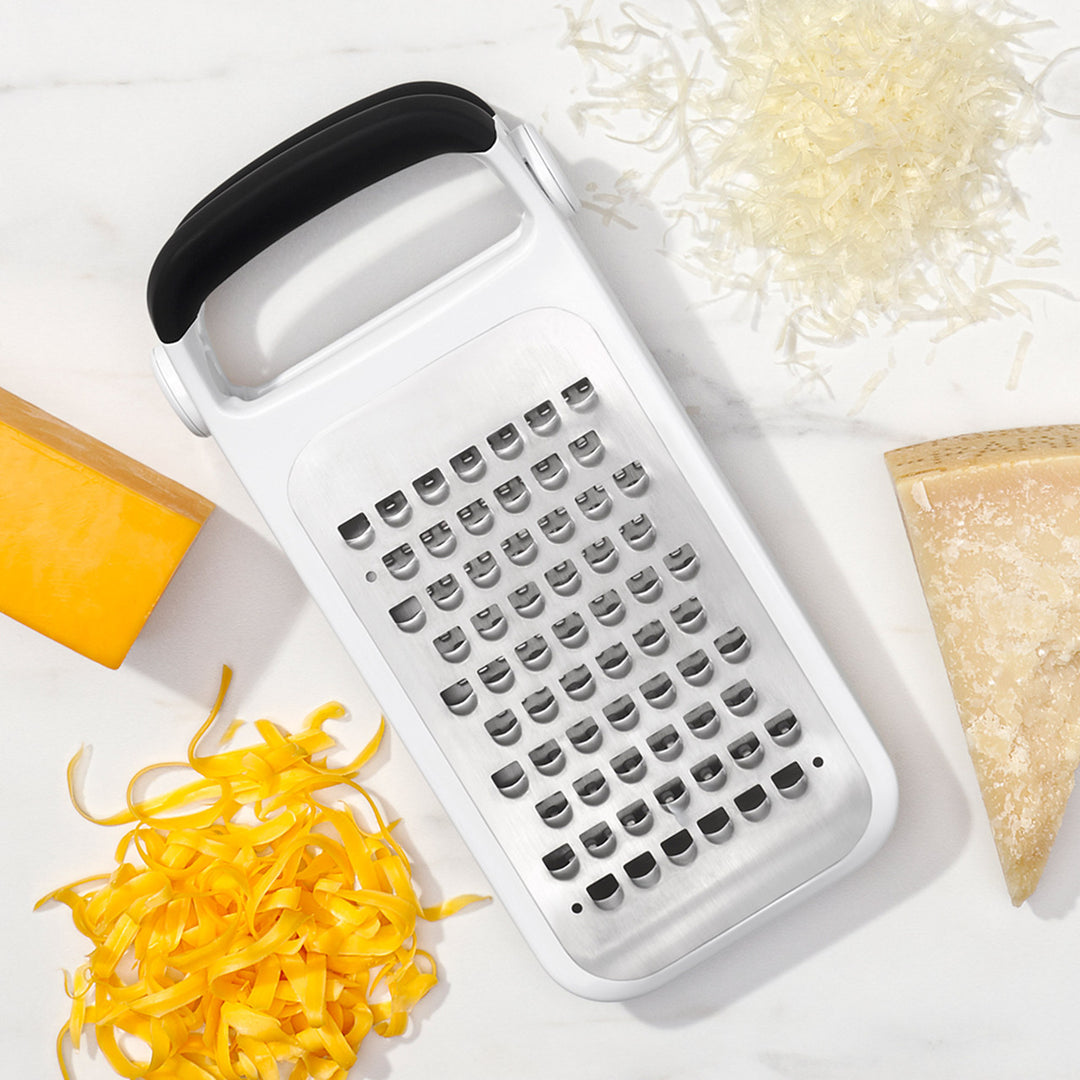 Box grater with shredded cheese and a piece of bread on a white background