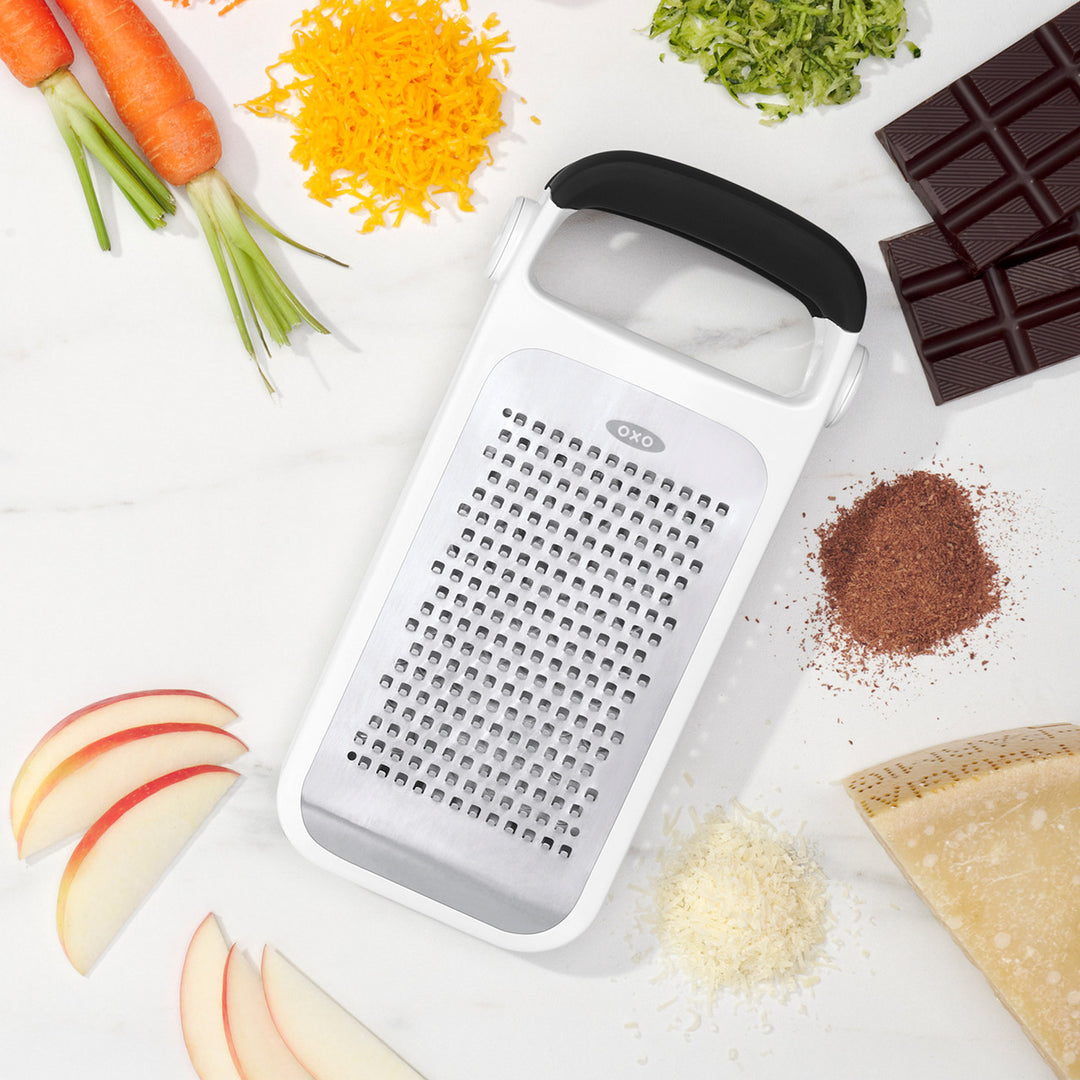 Oxo grater surrounded by various food items on a white surface