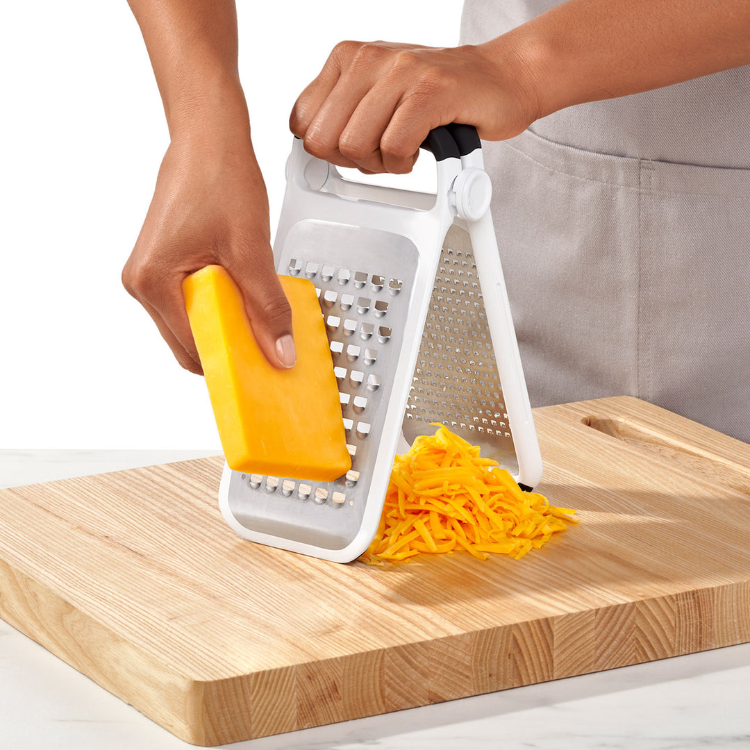 Person using a cheese grater on a block of cheese with shreds on a wooden cutting board.