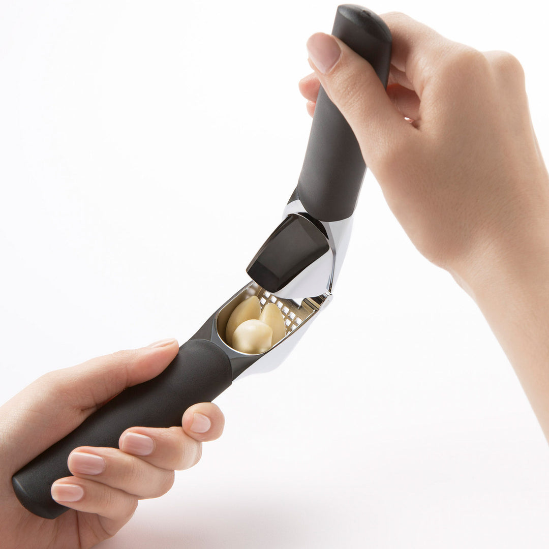 Hand holding a garlic press with cloves of garlic inside on a white background