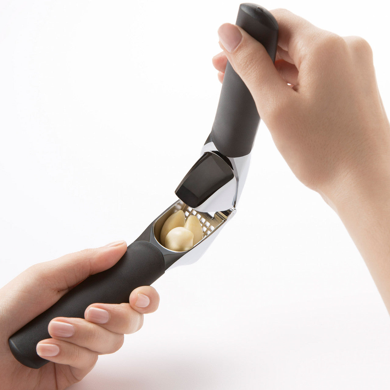 Hand holding a garlic press with cloves of garlic inside on a white background